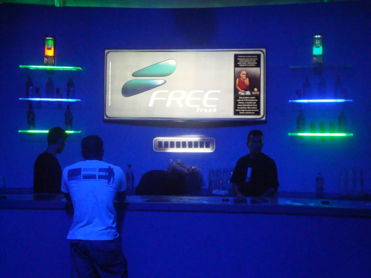 three men are standing in a blue lit bar