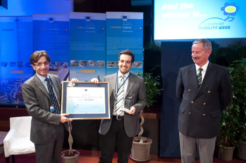 three men in business suits are holding a award plaque