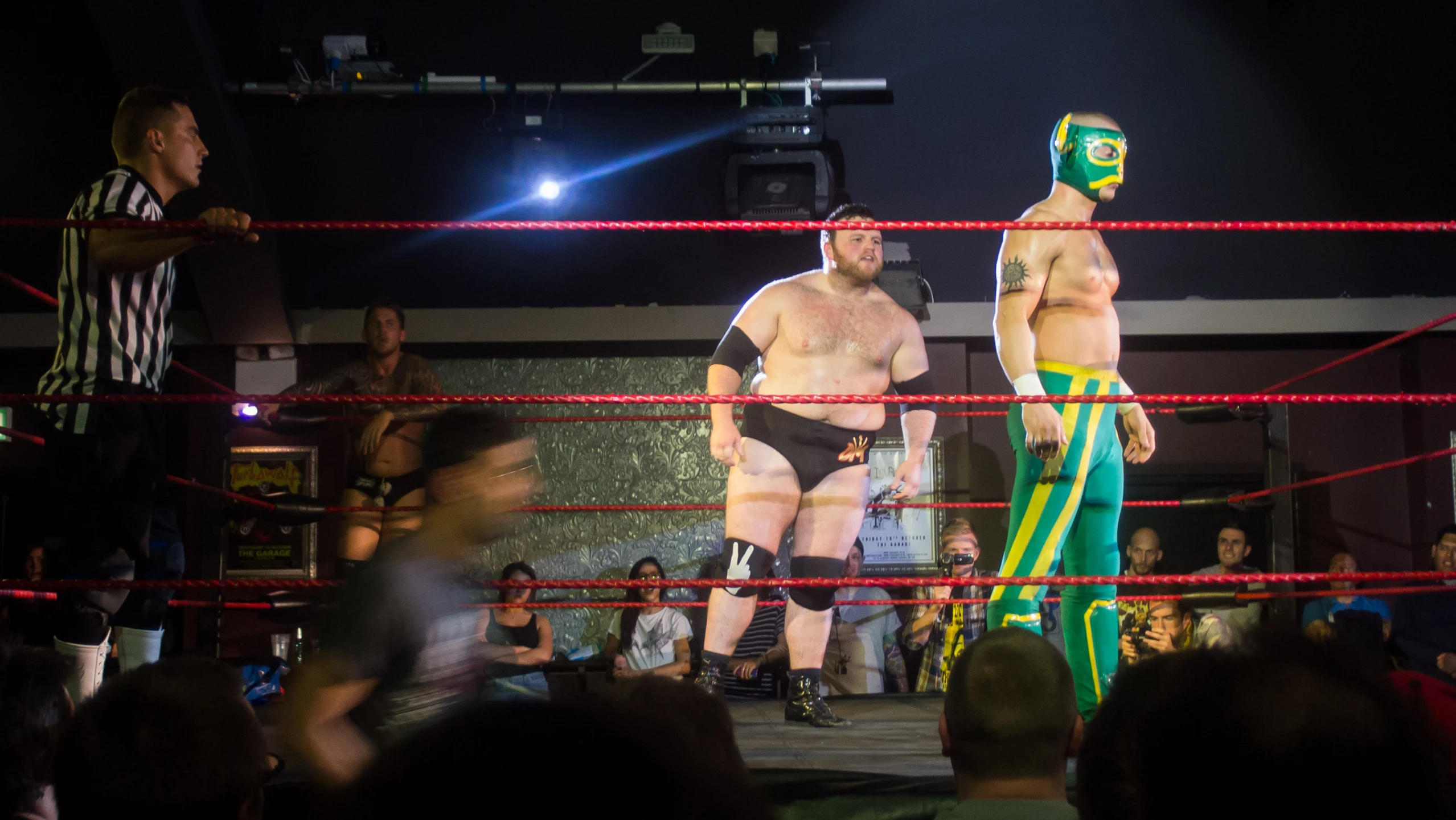 two men in wrestling clothes and one wearing a mask stand at a wrestling ring