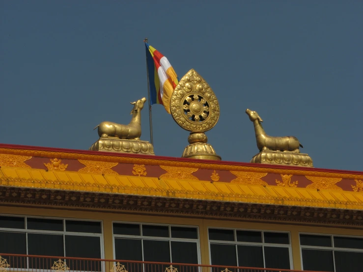 two golden statues, a flag and a gold helmet sit atop a building