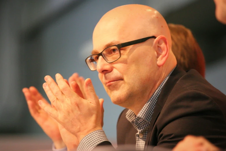 an older man wearing glasses clapping in front of someone