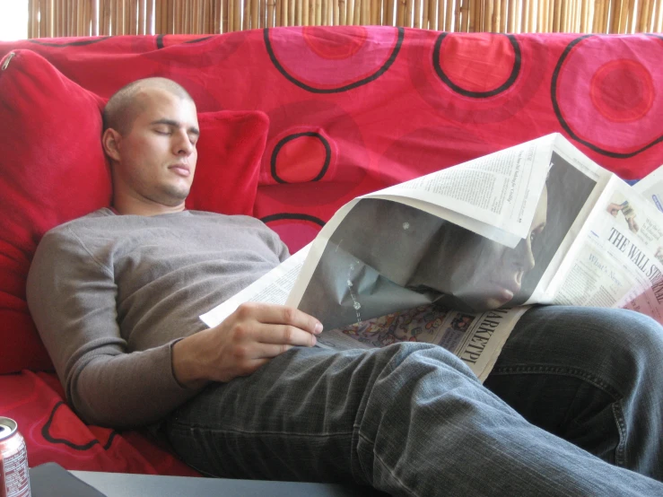 a man sitting on top of a red couch reading a newspaper