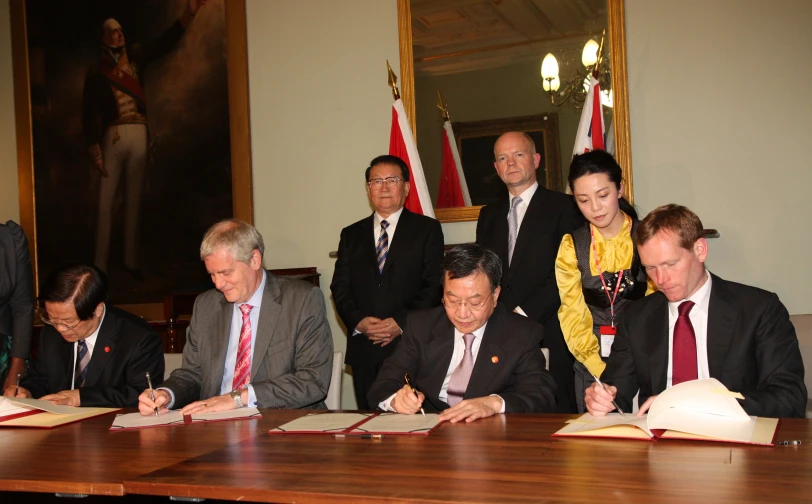 men in suits sitting at a table signing documents