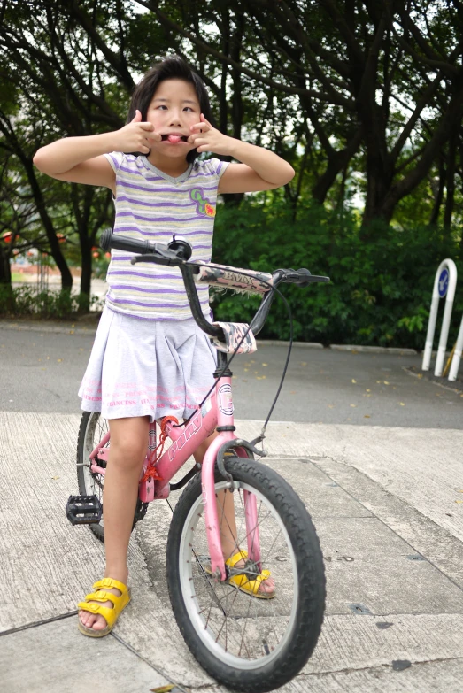 a  rides a pink bicycle with her finger in her mouth