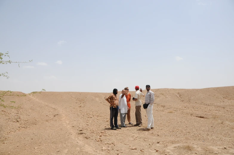 three men and one woman are standing in the sand