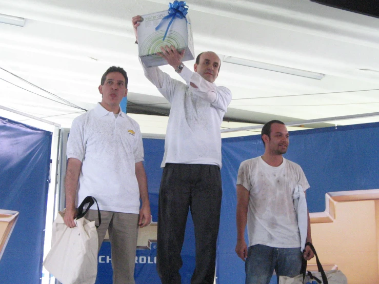 three men stand on the stage holding up boxes