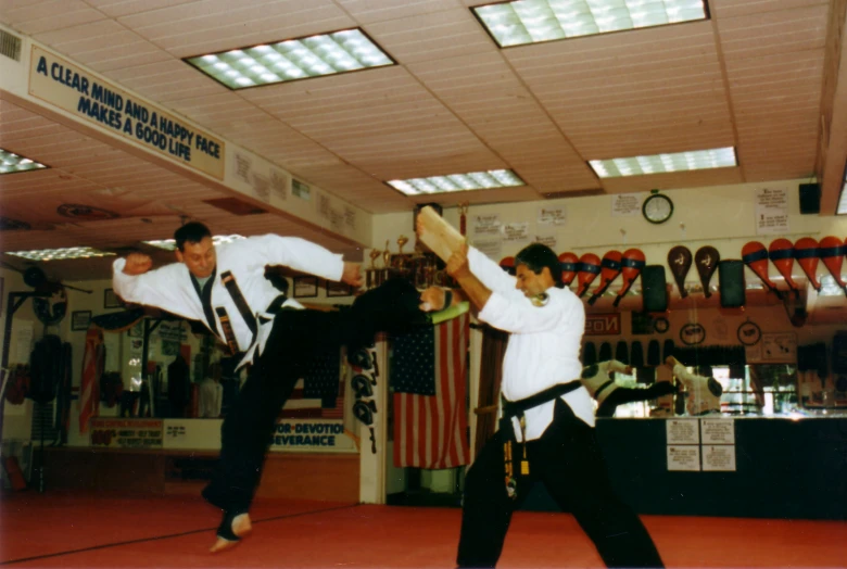 a man standing in a room while kicking another man with a black belt