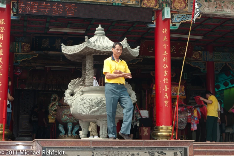 man in yellow shirt near fountain surrounded by red columns