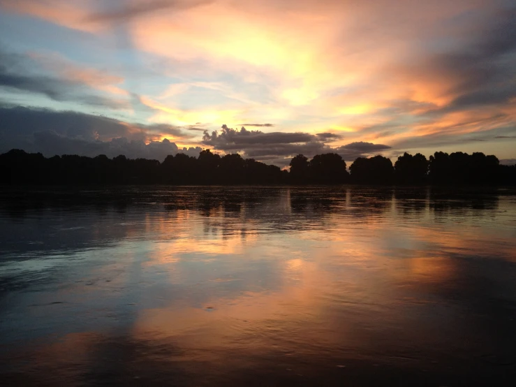 a sunset at the end of a river near the woods