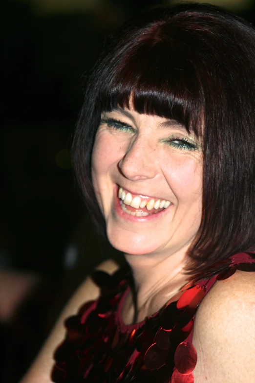a smiling woman with blunt bangs and a dark red dress