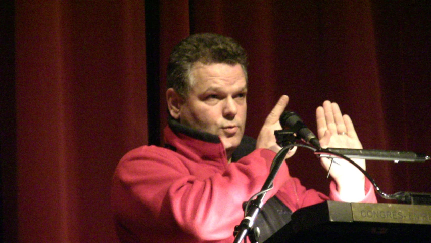 a man in red and black jacket giving a speech