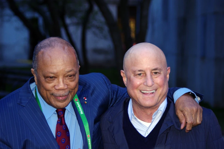 two men, one in business attire, smile at the camera