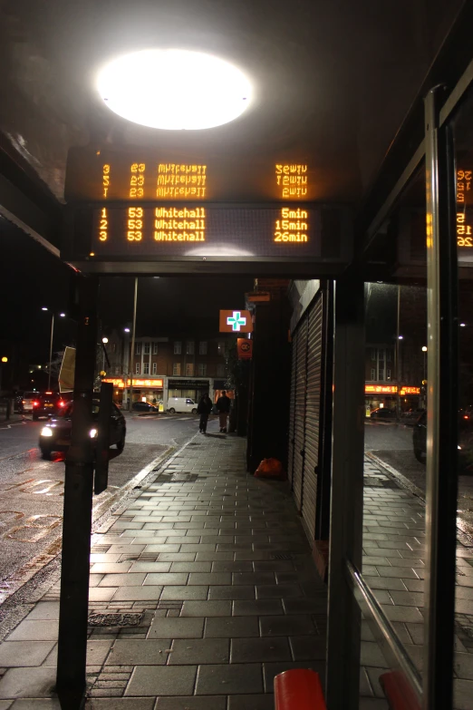 a lit up bus stop with a sign in the middle of it