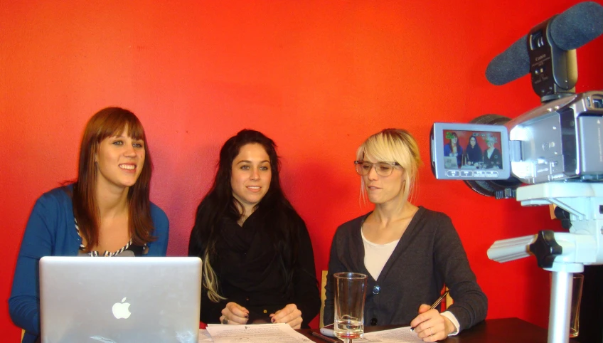 three woman are gathered in front of a laptop on a desk