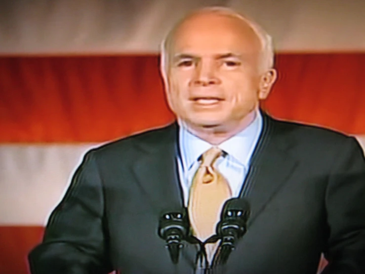 an old bald man giving a speech at a podium