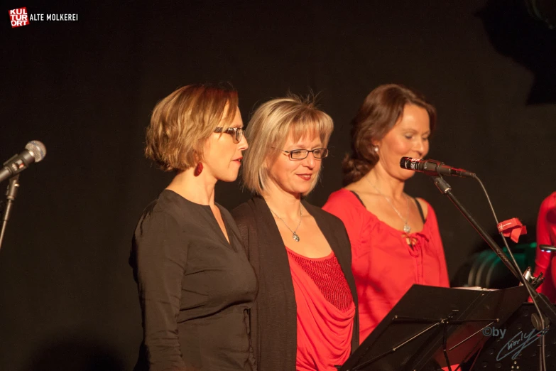 three women are singing together near a microphone