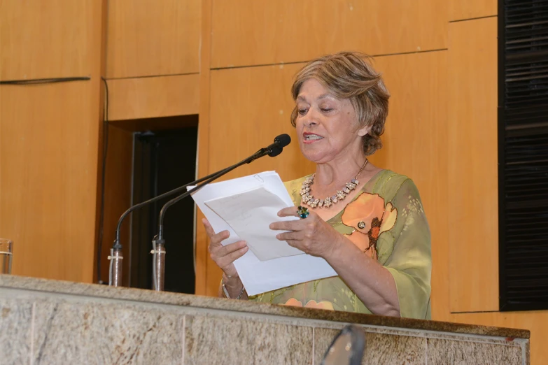 an old woman is giving a speech and holding her papers