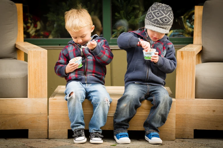 two little s sitting on a bench eating soing