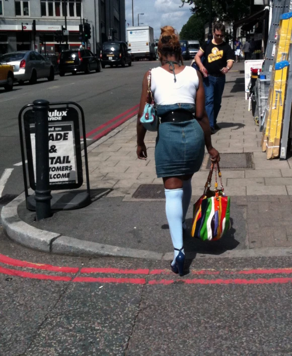 a woman wearing a dress and holding a purse walking down the street