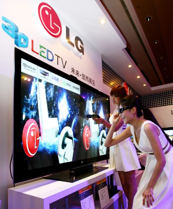 two woman stand looking at a television with an advertit in front