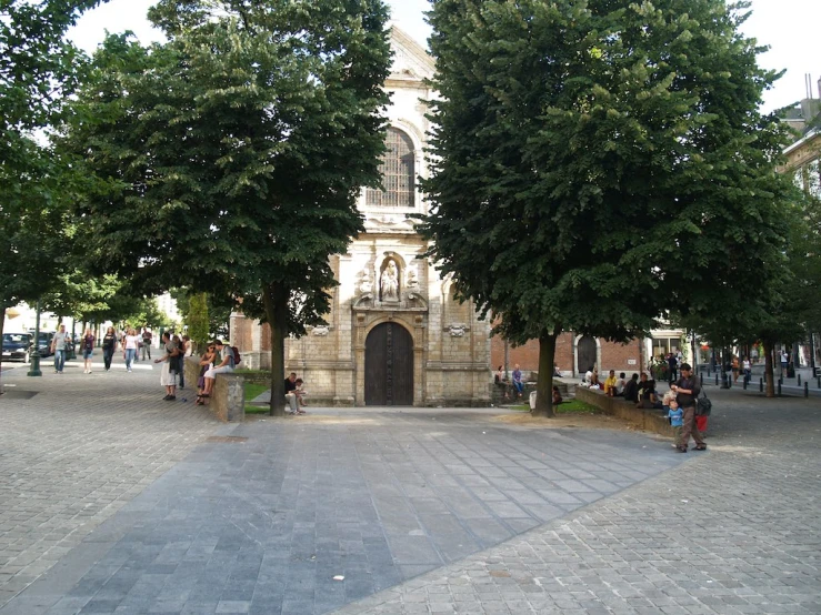 a group of people standing under trees next to a church