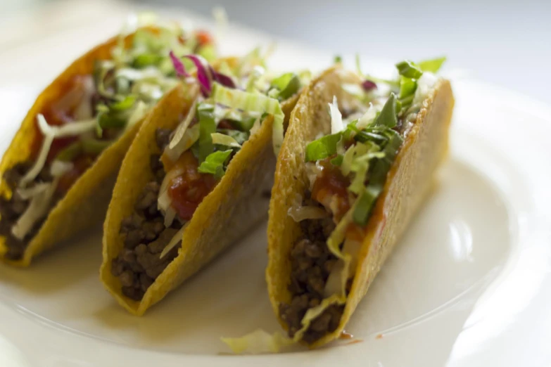 three tacos on a plate with lettuce, tomato and other toppings