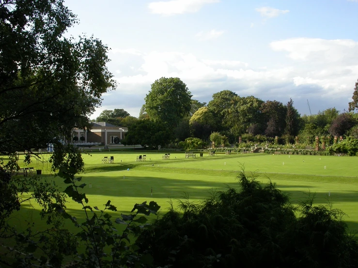 a green grass field and trees with people in the distance