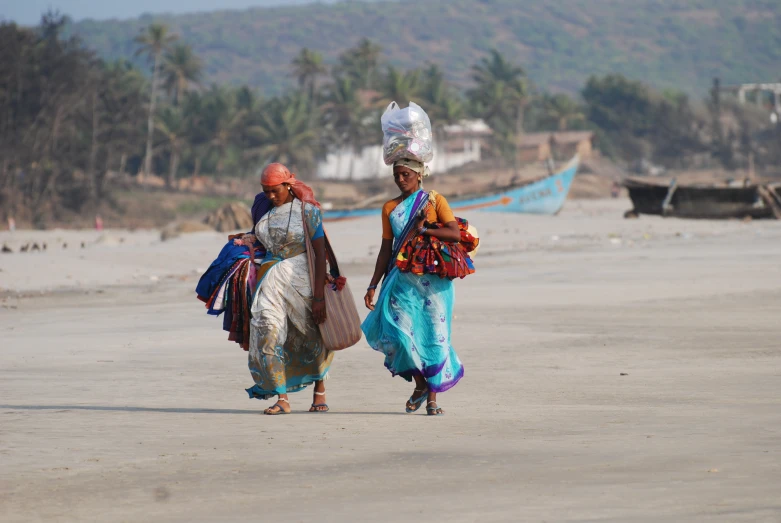 two women walking on a beach carrying goods