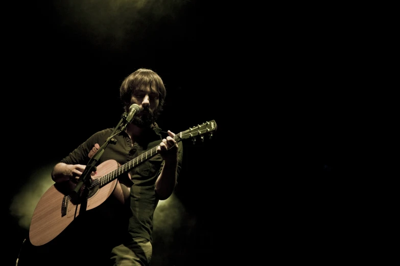 man holding guitar playing at dark stage in performance