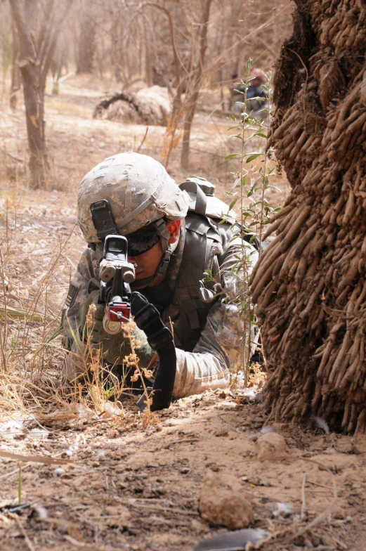 a soldier crouches in the woods taking pictures of an animal