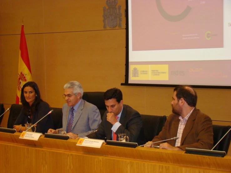 five people at a table are listening to a speaker