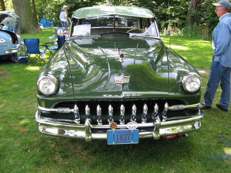 people are standing around a green classic car