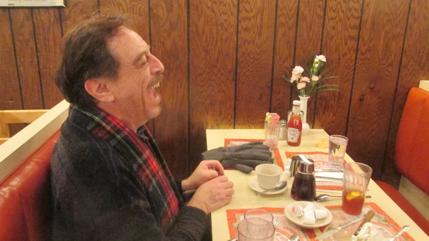 an older man eating at a table with his hands over his mouth