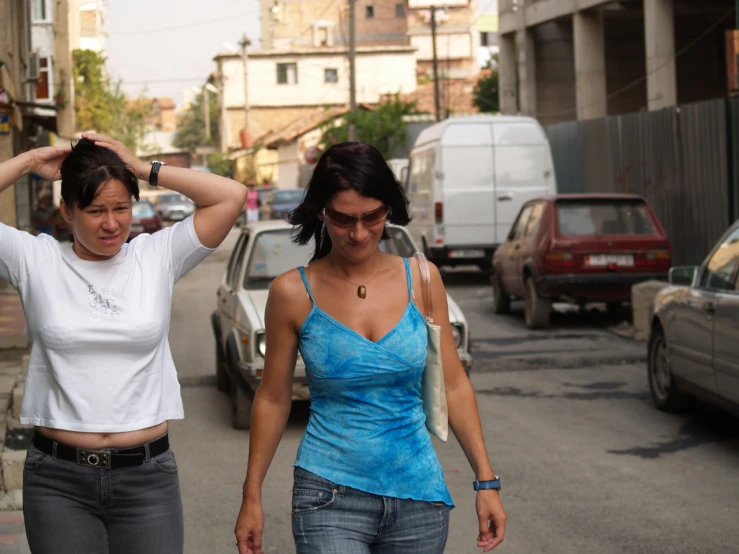 two women walking down a street, one has her hand on her hair