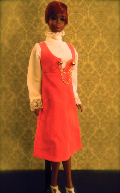a doll in an orange dress with gold necklaces