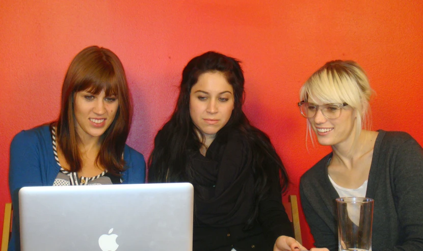 three girls sitting around each other with a computer in front of them