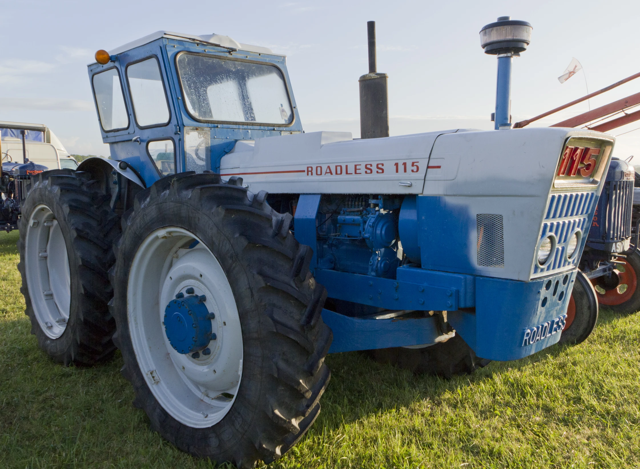 blue and white tractor parked on grass with other equipment in the background