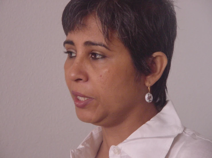 the head and shoulders of a woman with a white on up shirt, short black hair, and earrings