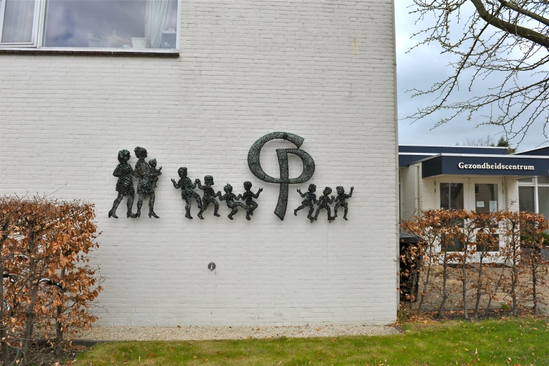 this white building has a unique metal wall sculpture depicting a group of people, as well as letters and symbols
