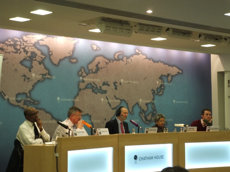 panel of men at a conference with an old world map behind them