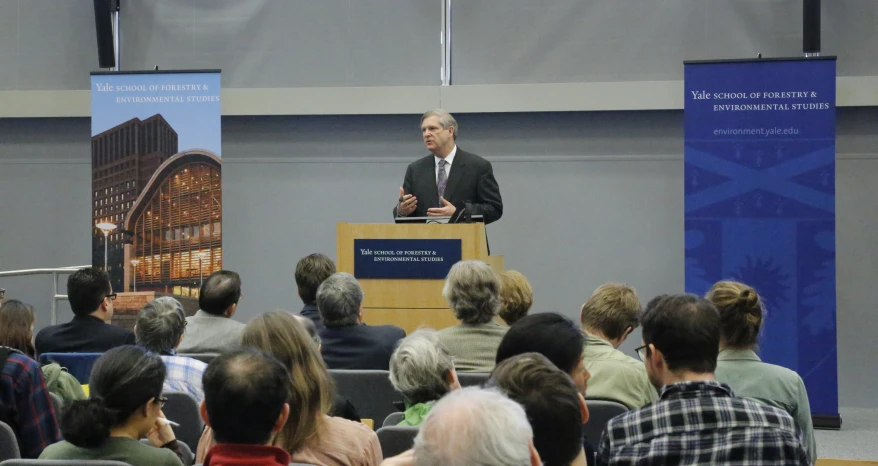 a man is giving a talk at a podium surrounded by people