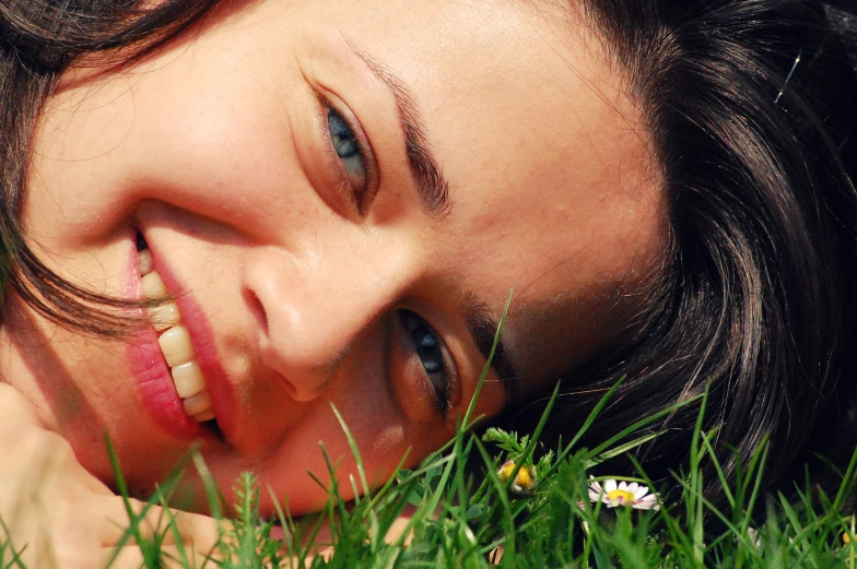 a woman laying in the grass with her head resting on the end of a toothbrush