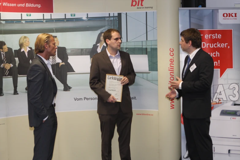 three men stand in front of a big poster