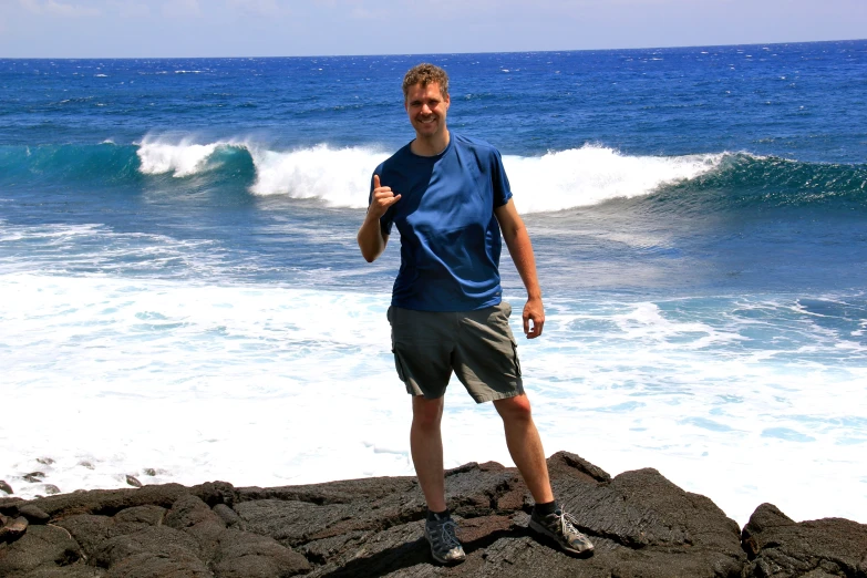 man standing on rock at the edge of the water with wave in background