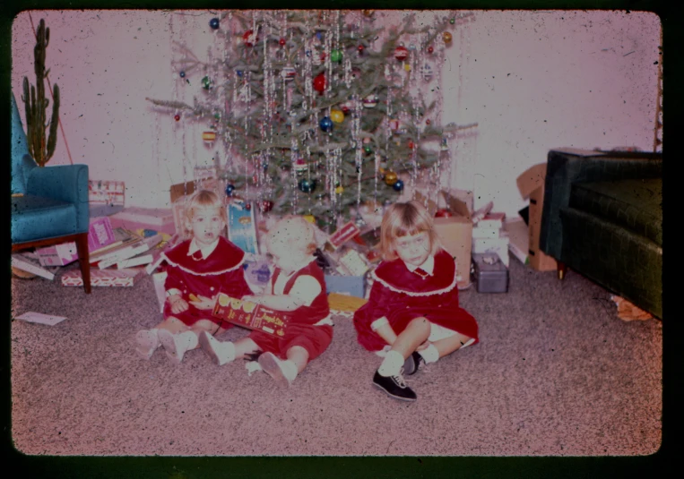 three girls sitting in front of a christmas tree