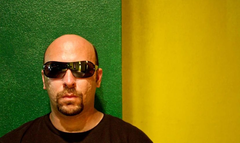 a balding man wearing sunglasses is next to a green and yellow wall