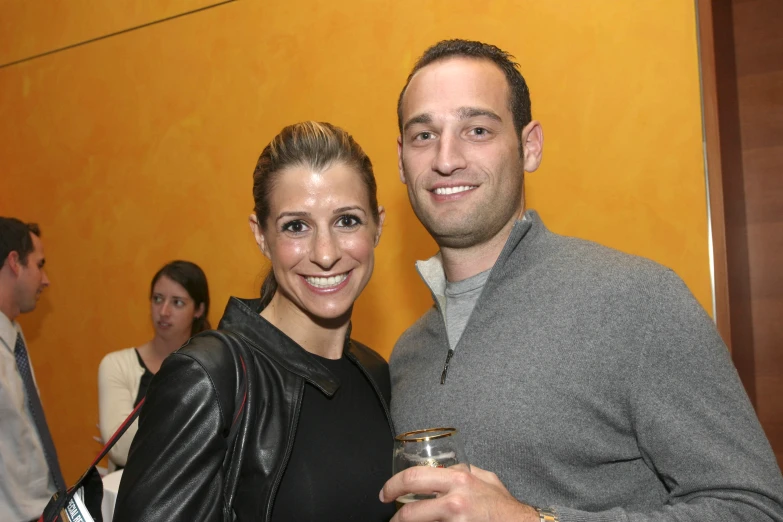 a smiling woman holds a drink next to a man holding another mans arm