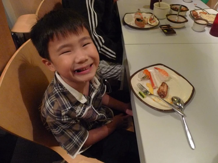 a young child sits at a table and smiles