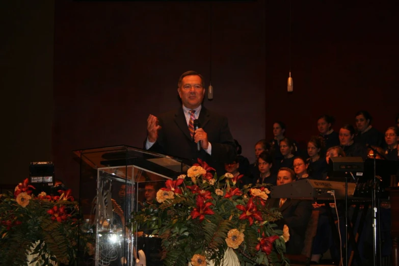 a man in a suit speaking at a podium with others seated