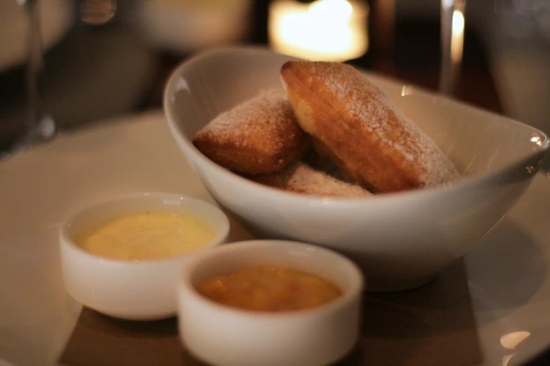 powdered sugary pastries in a white bowl with two small bowls full of mustard